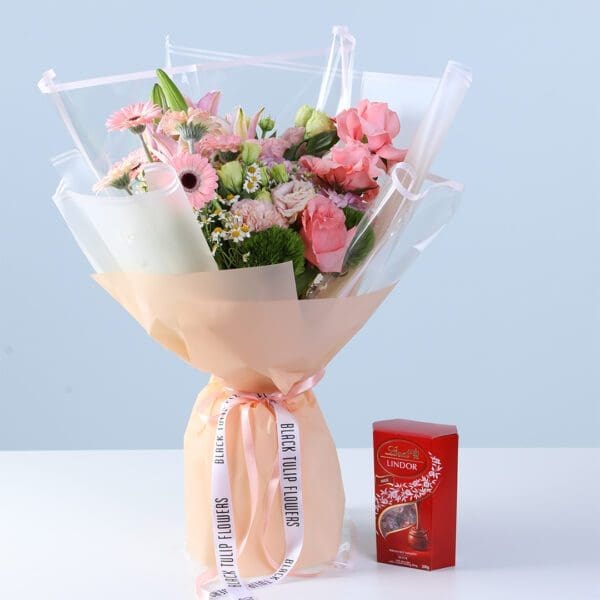 graceful-pink-celebration-bouquet-with-lindt Graceful Pink Celebration Bouquet with Lindt featuring pink gerberas, roses, lilies, hydrangea, and seasonal flowers arranged with chocolate for gifting