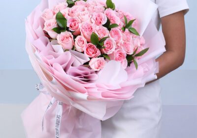 40 stem light pink rose bouquet with ruscus arranged in a full and graceful design, wrapped in a pink sheet and tied with a white satin ribbon
