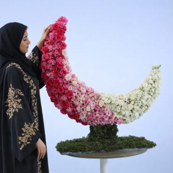 Crescent-shaped floral sculpture made of pink, white, and blush roses on a green base