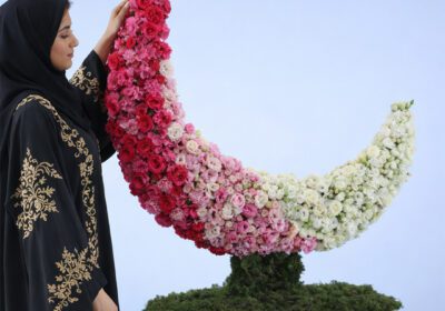 Crescent-shaped floral sculpture made of pink, white, and blush roses on a green base