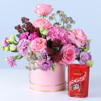 Premium Pastel Bloom Box with Lindt chocolates featuring pink roses, hydrangea, lisianthus, and seasonal flowers arranged in a pink hatbox