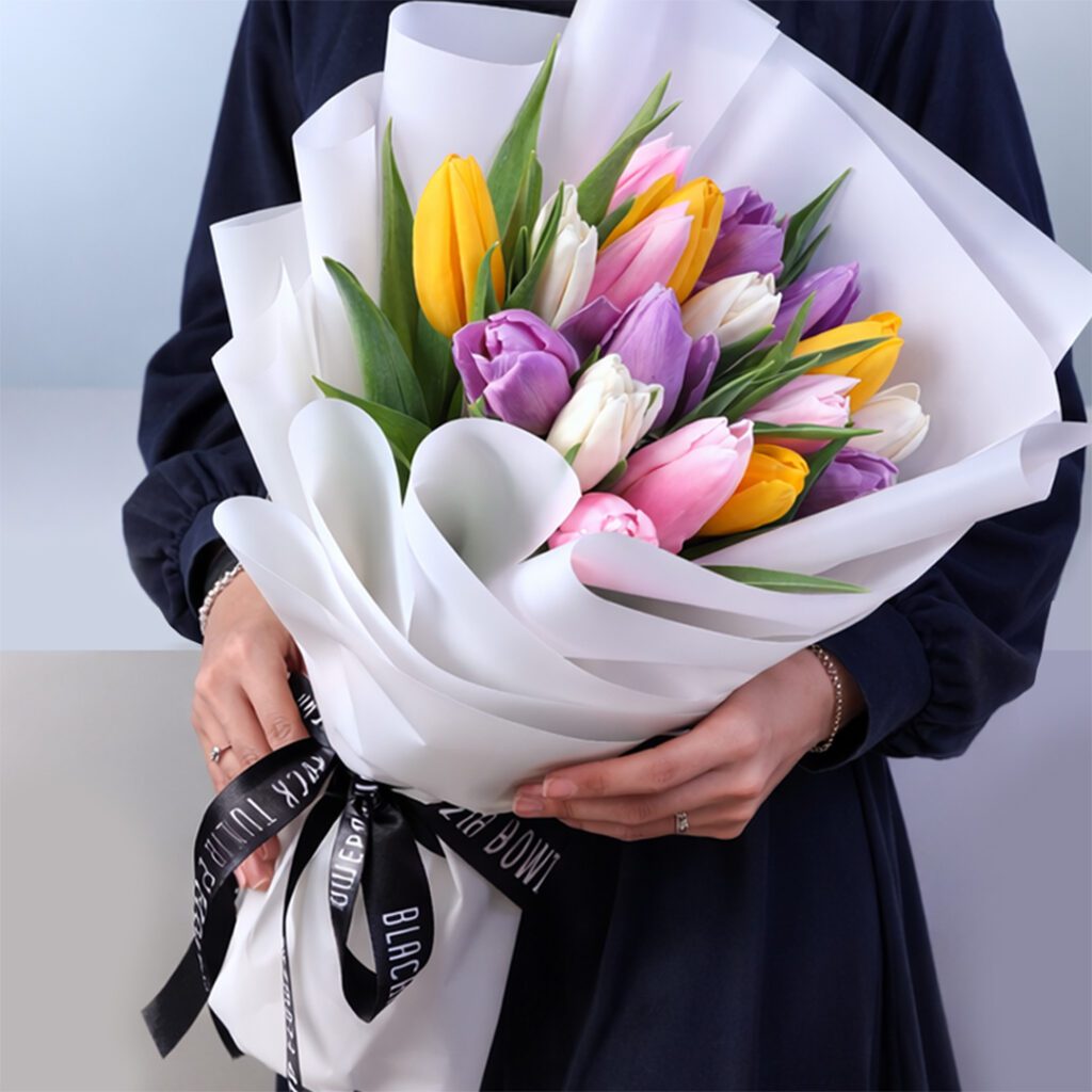 Colorful mixed tulip bouquet wrapped in white paper with a premium ribbon, featuring vibrant fresh tulips