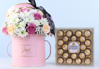 Signature Peach Bloom Ferrero 24 Pcs Combo featuring purple roses, peach roses, lisianthus, chrysanthemums, and Ferrero chocolates arranged in a round pink box