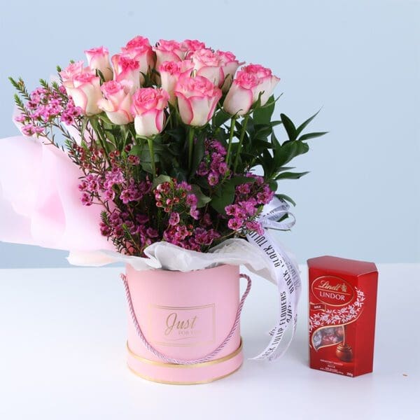sweet-bloom-surprise-box-with-lindt-chocolate Sweet Bloom Surprise Box with Lindt featuring double pink roses, wax flowers, greenery, and Lindt chocolates arranged in a pink luxury box for gifting