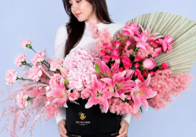 Designer Rose Luxe Box featuring hydrangea, lilies, roses, carnations, and spray roses in soft pink tones arranged in a premium black luxury box with dried foliage accents