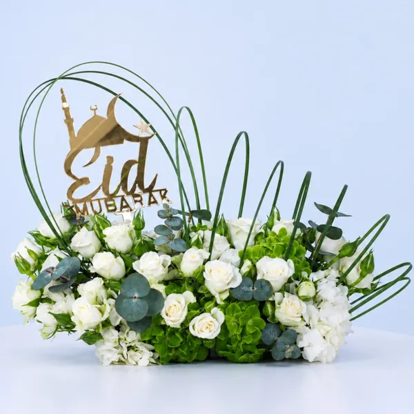 eid-harmony-floral-arrangement Eid Harmony Floral Arrangement featuring white roses, white and green hydrangeas, eucalyptus, and arched steel grass with an Eid topper for festive décor