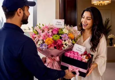 A delivery executive presents a colorful birthday flower bouquet and a pink rose gift box to a smiling woman at her doorstep in Doha, celebrating a special birthday surprise