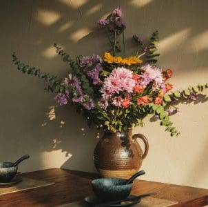 brown ceramic vase with a handle holds a vibrant and somewhat wild bouquet of flowers.
